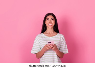 Photo Of Gorgeous Young Chinese Lady Hold Gadget Look Up Empty Space Poster Dressed Trendy White Clothes Isolated On Pink Color Background