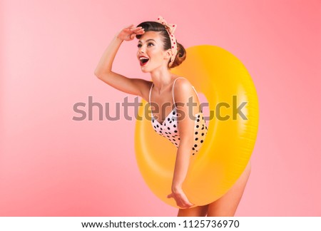 Photo of gorgeous young pin-up woman isolated over pink background wall in swimwear with inflatable ring. Looking aside.