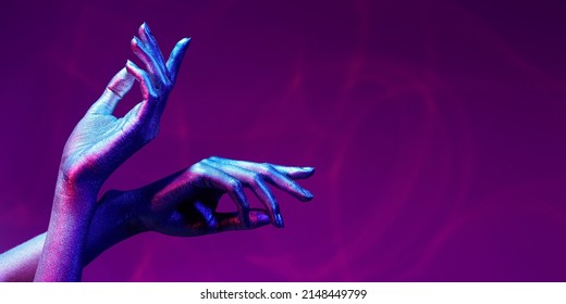 Photo of graceful thin hands with sparkling silvery skin in bright neon blue and pink lighting. Body painting, body art. Glitter makeup. Beauty industry, cosmetology. Copy space.