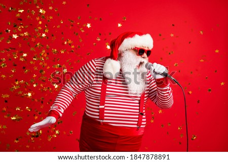 Photo of grandpa grey beard hold mic open mouth scream sing song karaoke wear santa claus x-mas costume suspenders sunglass striped shirt cap isolated red color background