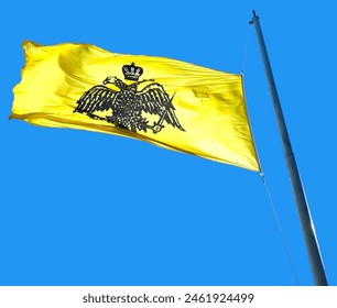 Photo of the Greek Orthodox Church flag waving against a clear blue sky.