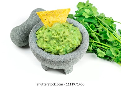 A Photo Of Guacamole Sauce In A Molcajete, Traditional Mexican Mortar, On A White Background, With A Pestle. A Bunch Of Cilantro, A Nacho Chip, And A Place For Text