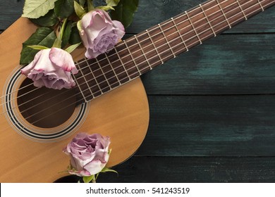 A photo of a guitar neck with tender pink roses, on a dark wooden background with copyspace