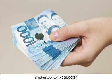 Photo of hand holding folded bundle of blue money in cash of one thousand Philippines peso. Giving bribe or graft, paying bills or getting salary. Payment day!