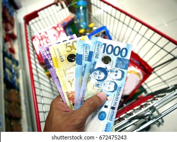 Photo of a hand holding Philippine Peso bills while inside a grocery store