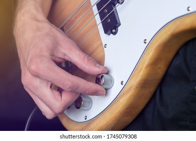 Photo Of A Hand Hand Twisting The Volume Knob With Its Fingers Of The Natural Wood Color Electric Bass Guitar On Black Background Close Up