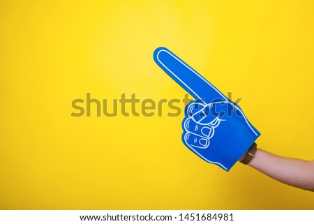 Photo of a handsome arm,  wearing a big blue fan glove, over isolated yellow background 