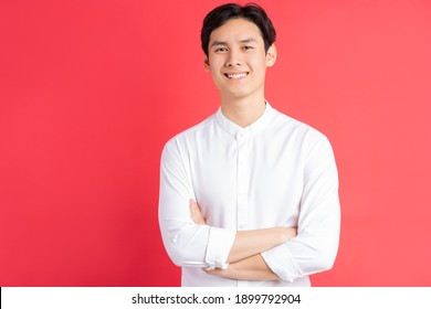 A photo of a handsome Asian man standing with his arms crossed on a red background
