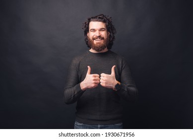 Photo of handsome bearded man showing thumbs up standing over black background.