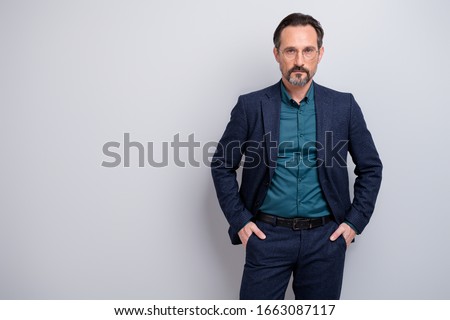 Photo of handsome business man skilled professional self-confident stand hands in pockets not smiling formalwear blazer shirt trousers blue suit specs isolated grey color background