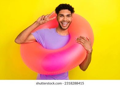 Photo of handsome cheerful excited person hold inflatable ring hand fingers demonstrate v-sign isolated on yellow color background - Shutterstock ID 2318288415