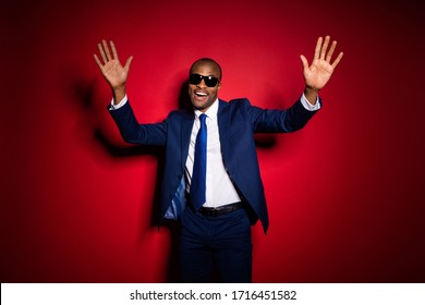 Photo of handsome dark skin business guy cool macho corporate party event raise hands meet colleagues wear sun specs blue formalwear suit tuxedo isolated red burgundy background