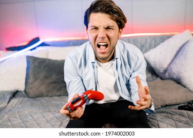 Photo of handsome excited guy sitting at comfy sofa, quarantine stay home gamer holding play station joystick, good mood fifa championship, Unhappy gamer player dissatisfied with video game.