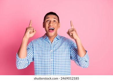 Photo of handsome good mood guy wear plaid shirt showing two fingers up emtpy space isolated pink color background