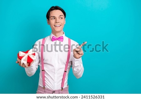 Photo of handsome guy point look interested empty space hold heart box dressed stylish pink garment isolated on aquamarine color background