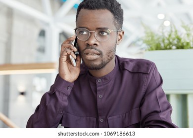 Photo of handsome serious dark skinned male solves during telephone consultancy, tries to explain his idea, talks with costumer support, has business conversation. People and communication concept - Shutterstock ID 1069186613