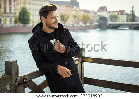 Photo of handsome smiling man in black coat in autumn scenery