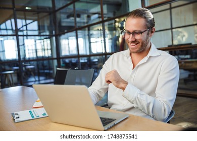 Photo of handsome smiling man wearing eyeglasses working with laptop while sitting at table in modern office - Shutterstock ID 1748875541