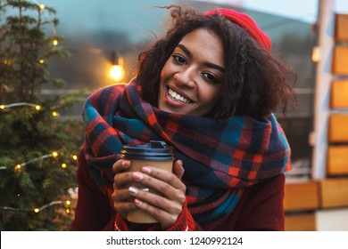 Photo of a happy african young woman standing posing outdoors winter concept drinking coffee. ภาพถ่ายสต็อก