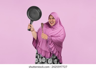 Photo of happy  Asian Muslim woman housewife wearing apron holding frying pan with spatula isolated on pink background. Housekeeping concept - Powered by Shutterstock