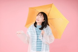 Photo D'une Femme Asiatique Heureuse, Portant Un Imperméable, Se Trouve Sous Un Parapluie Jaune Sur Fond Rose