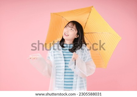 Photo of happy asian woman, wear raincoat stands under yellow umbrella against pink background