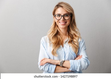 Photo of happy blond businesswoman wearing eyeglasses smiling and standing with hands crossed isolated over gray background