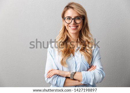 Photo of happy blond businesswoman wearing eyeglasses smiling and standing with hands crossed isolated over gray background