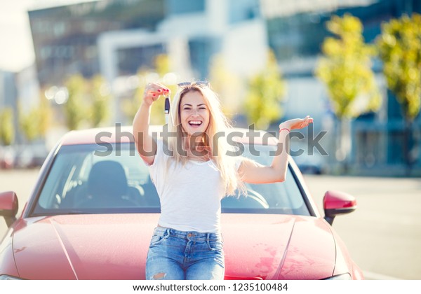 Photo of happy blonde woman with keys standing near
red car