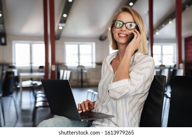 Photo of happy blonde woman wearing eyeglasses talking on cellphone while sitting in conference hall