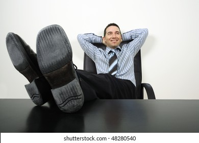 Photo of a happy businessman reclining with his feet up and hands behind his head.