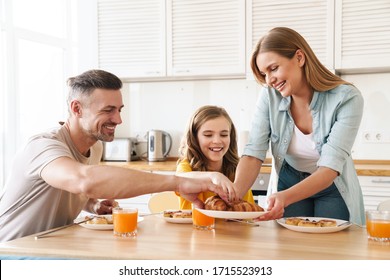 Photo of happy caucasian beautiful family smiling and eating croissants while having breakfast in modern kitchen - Powered by Shutterstock