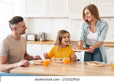 Photo of happy caucasian beautiful family smiling and eating croissants while having breakfast in modern kitchen - Powered by Shutterstock