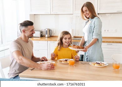 Photo Of Happy Caucasian Beautiful Family Smiling And Eating Croissants While Having Breakfast In Modern Kitchen