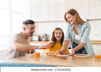 Photo Of Happy Caucasian Beautiful Family Smiling And Eating Croissants While Having Breakfast In Modern Kitchen