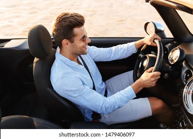 Photo Of Happy Caucasian Man Wearing Sunglasses Driving Convertible Car By Seaside At Sunrise