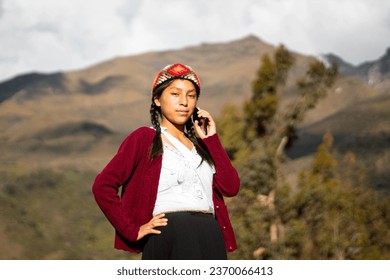 Photo of a happy Caucasian peasant woman talking on a smartphone wearing a hand-woven chopa. Peasant woman with typical Peruvian handmade clothing on a sunset in the Peruvian Andes. Woman using mobile