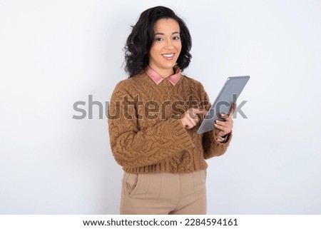 Photo of happy cheerful  beautiful woman wearing knitted sweater over white background hold tablet browsing internet