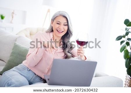 Photo of happy cheerful old woman look laptop talk webcamera drink wine indoors inside house home apartment