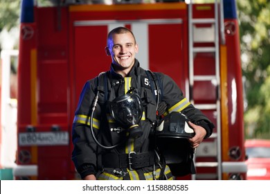 Foto de feliz bombero con máscara de gas y casco cerca del motor de bomberos