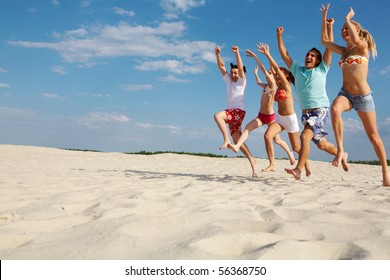 Foto von glücklichen Freunden, die den Sandstrand mit aufgewühlten Armen entlang laufen