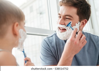 Photo of happy handsome father and son are applying shaving foam on their faces and smiling while shaving in bathroom స్టాక్ ఫోటో
