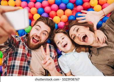 Photo of happy little child have fun with his parents in entertainment game center. Looking aside make selfie by phone showing peace gesture. - Powered by Shutterstock