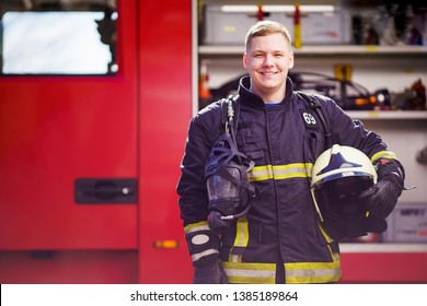 Photo of happy male firefighter with helmet in his hands against background of fire truck