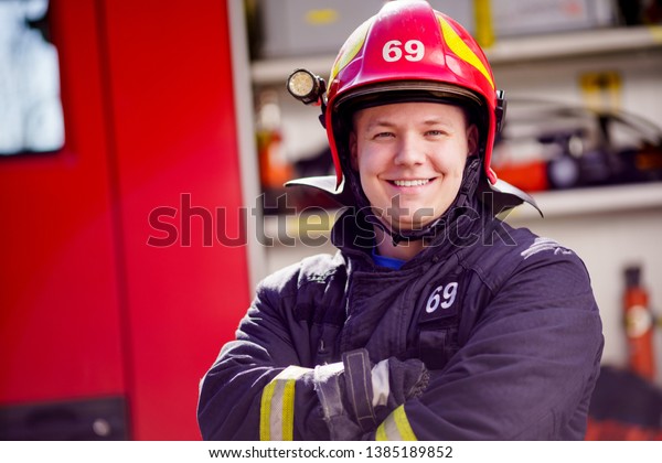 Photo of happy male firefighter in helmet on\
background of fire truck