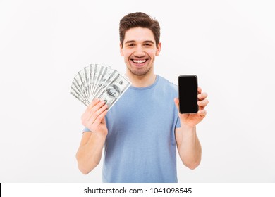 Photo Of Happy Man In Casual T-shirt Holding Fan Of Money In Dollar Banknotes And Mobile Phone In Hands Isolated Over White Wall