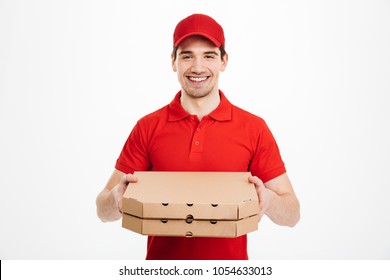 Photo of happy man from delivery service in red t-shirt and cap giving food order and holding two pizza boxes isolated over white background