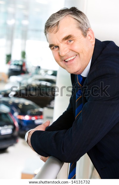 Photo of happy man leaning against\
balcony railing while looking at camera with\
smile