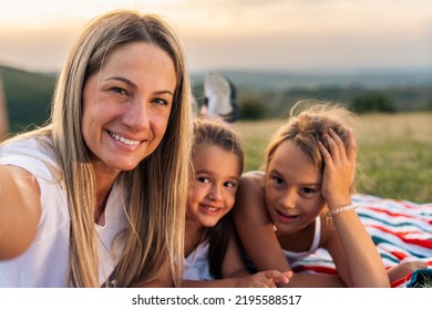 Photo Of Happy Mother And Daughters Smiling And Laughing Lying On Blanket In Park, They Posing For Photo.