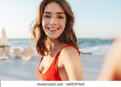 Photo of happy nice woman in red swimsuit smiling and taking selfie photo at luxury sunny beach - Powered by Shutterstock